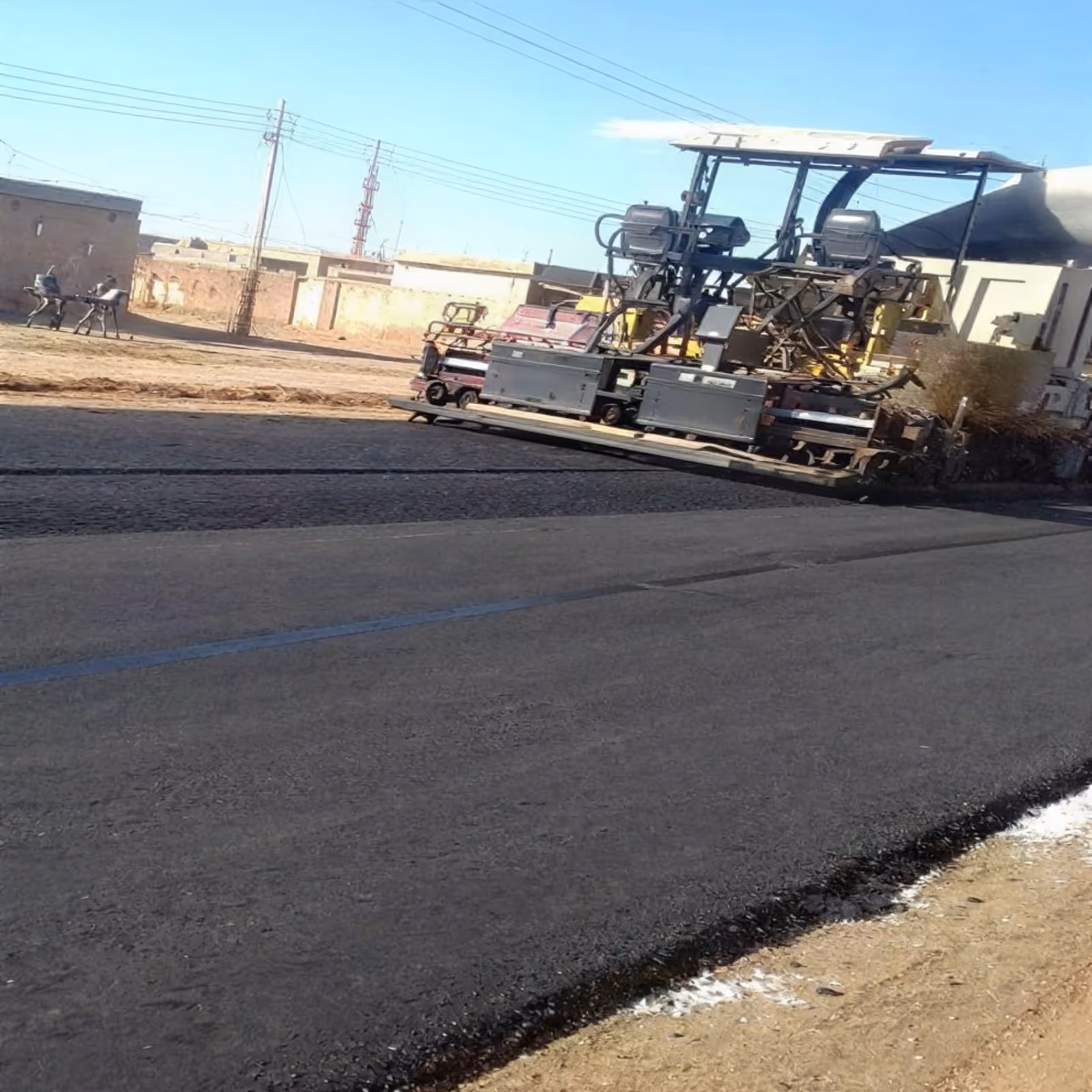 Asphalt paving works underway on Haj Youssef Road with machinery operating along the finished carriageway.